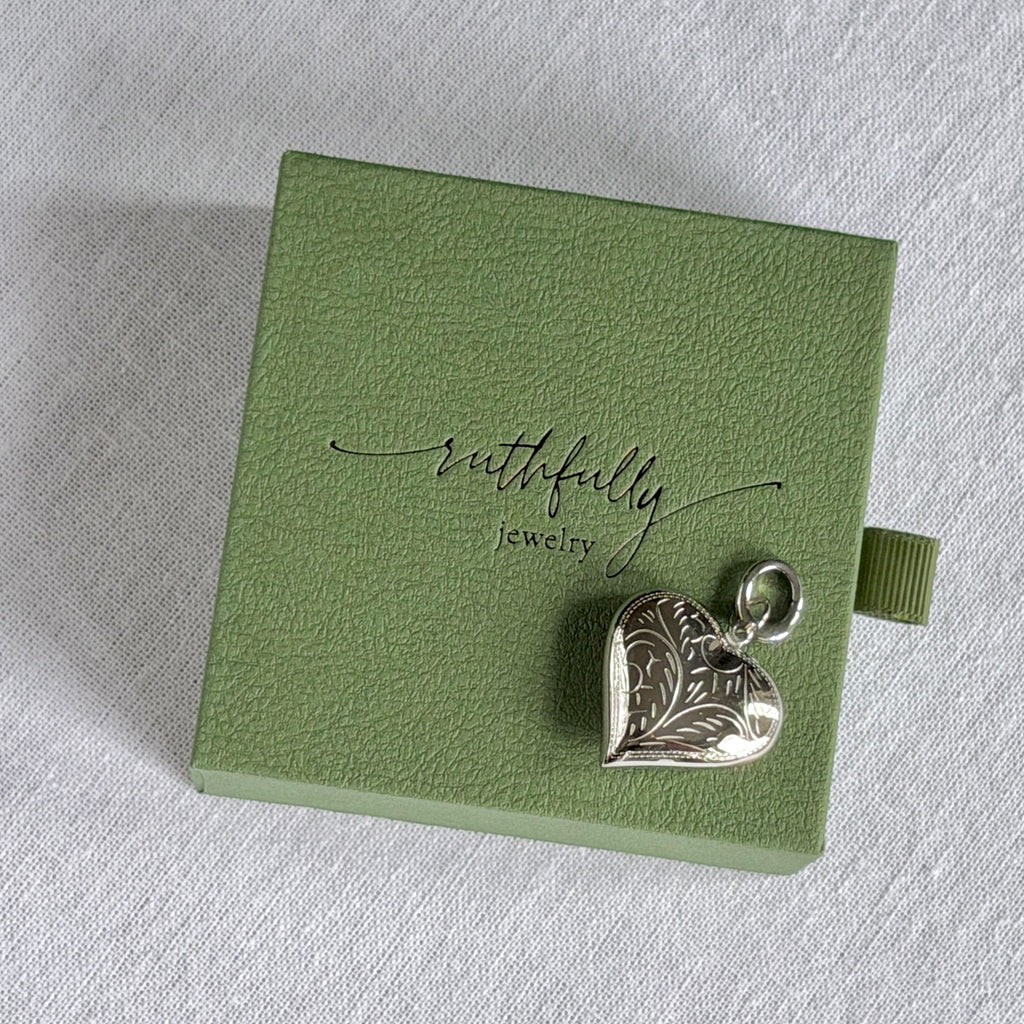 Silver heart-shaped pendant on a green jewelry box with 'ruthfully jewelry' branding.
