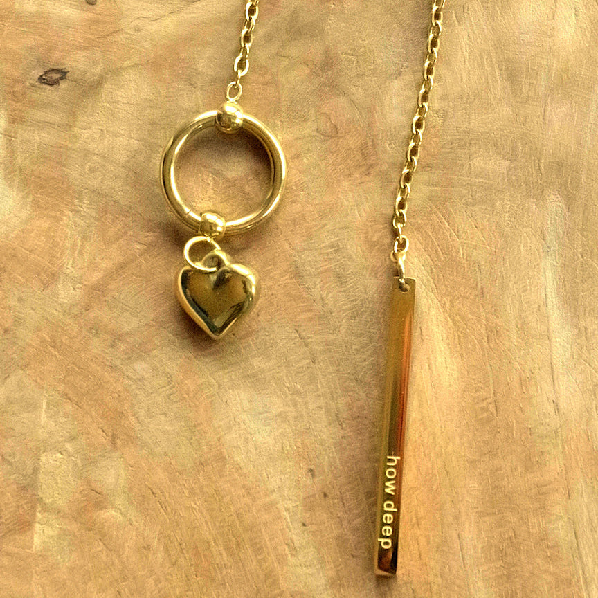 Gold necklace with heart charm and 'how deep' pendant on a wooden surface